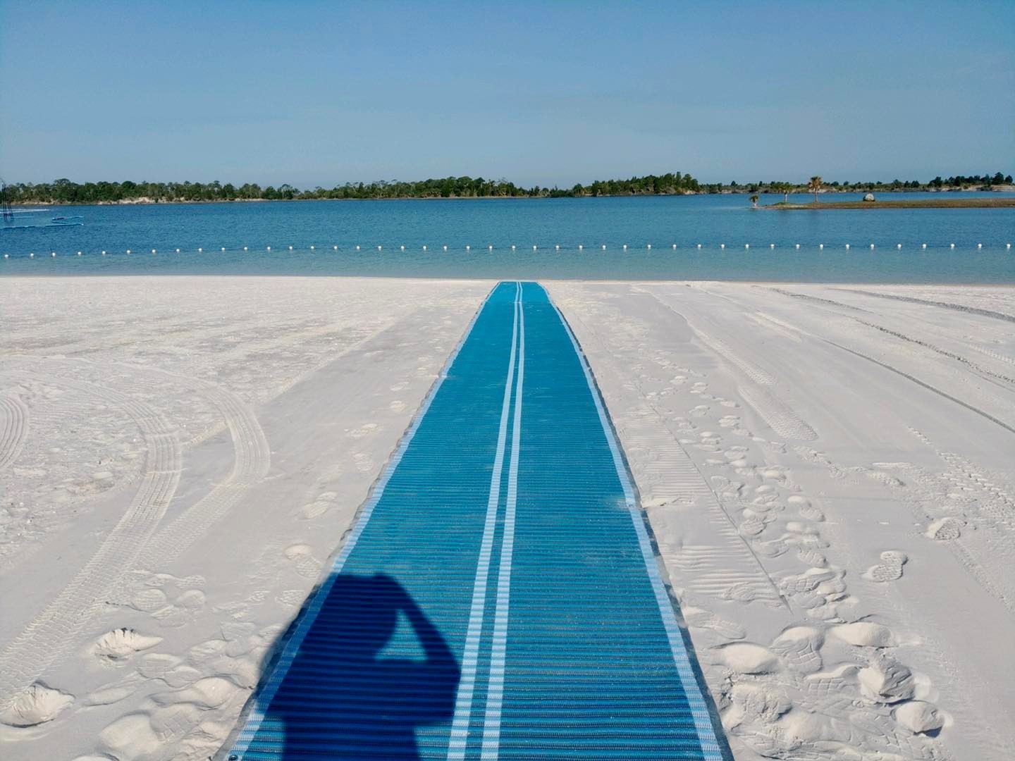 A blue access mat crosses white beach sand toward calm water.